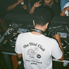 DJ operating equipment at a club event with 'The Dial Club' t-shirt
