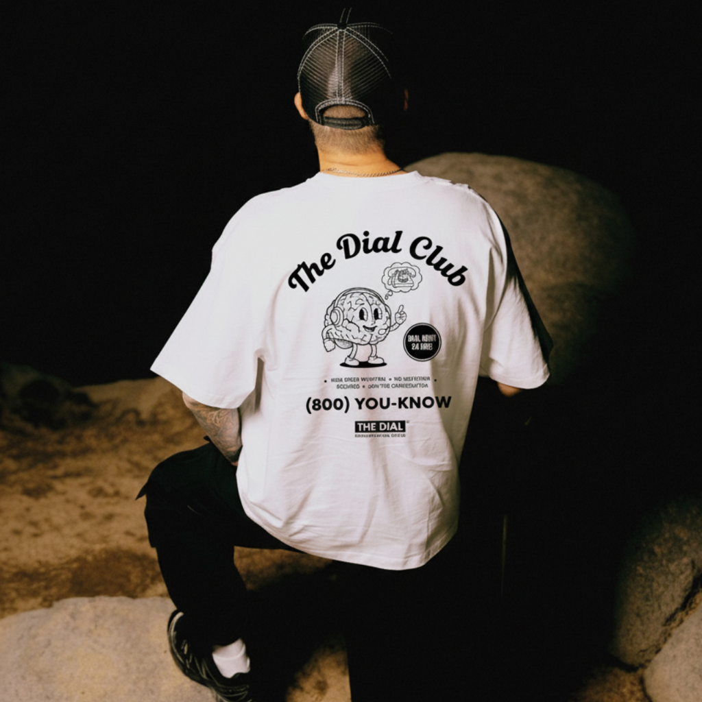 Person wearing a white t-shirt with 'The Dial Club' logo sitting on a stone wall.
